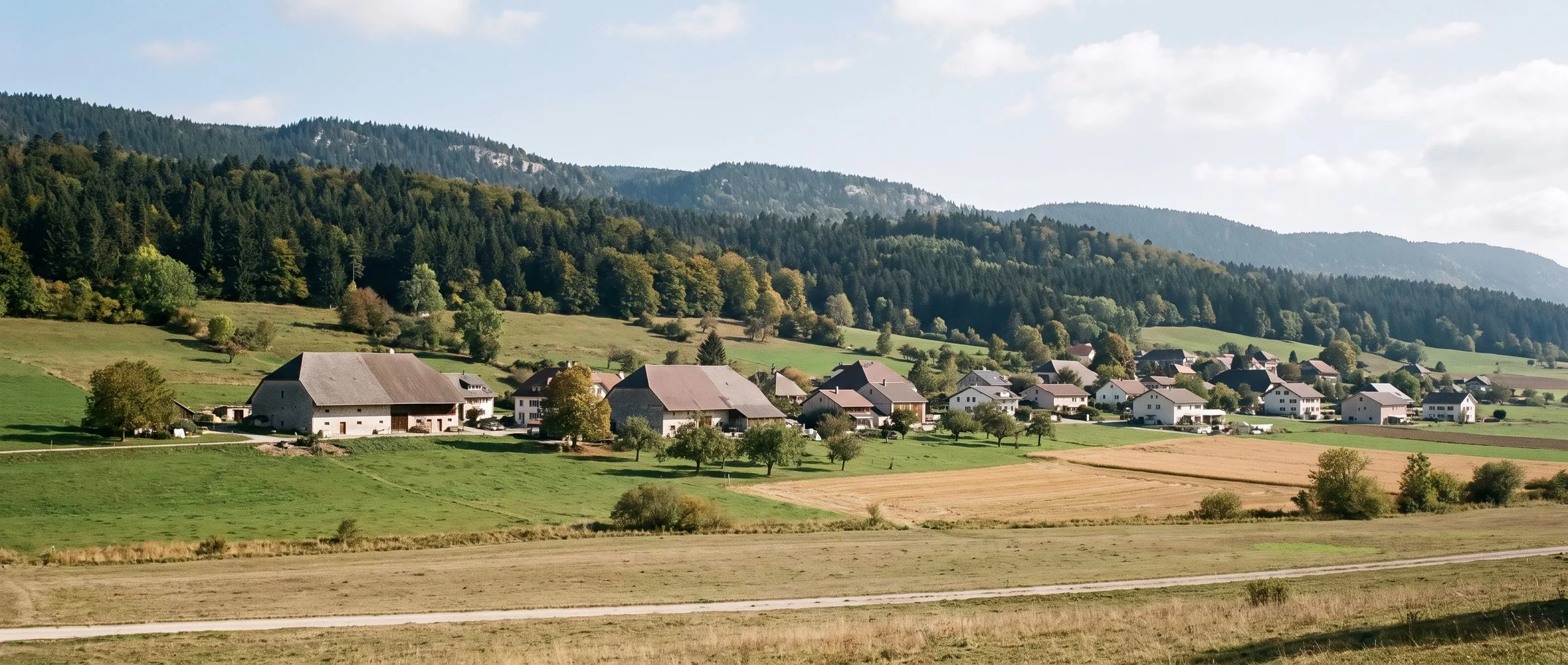 Le village de Chézard-Saint-Martin dans le Val-de-Ruz en septembre, fermes et maisons entourées de prés et de champs, au pied des pentes boisées du Jura, sans vignes.